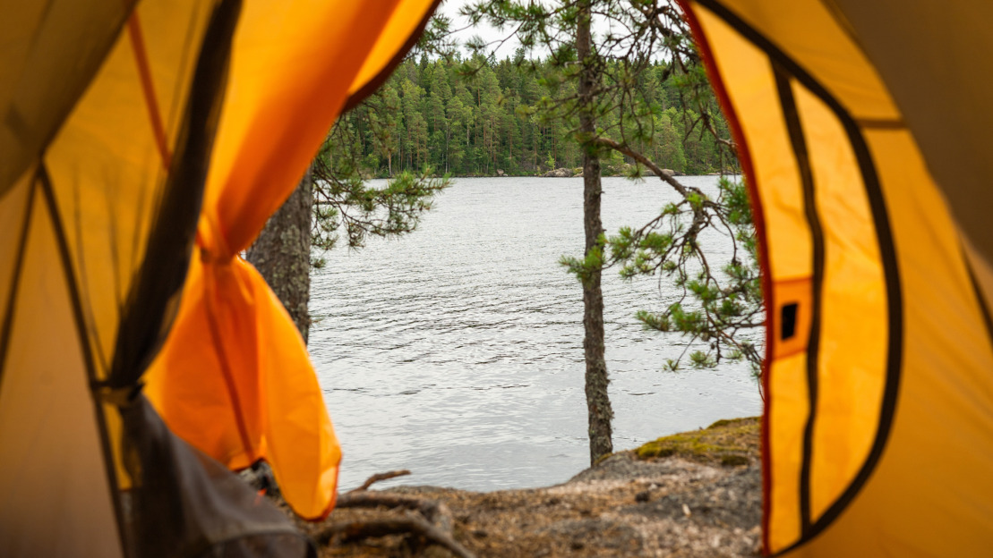 Kuva otettu teltan avoimesta oviaukosta, ulkona näkyy kalliota ja järvi.